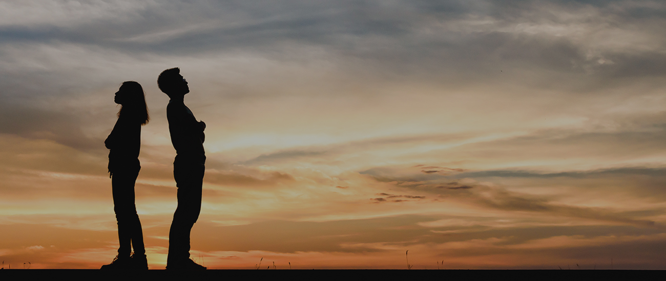 Silhouette of couple standing back to back in from of a sunset.