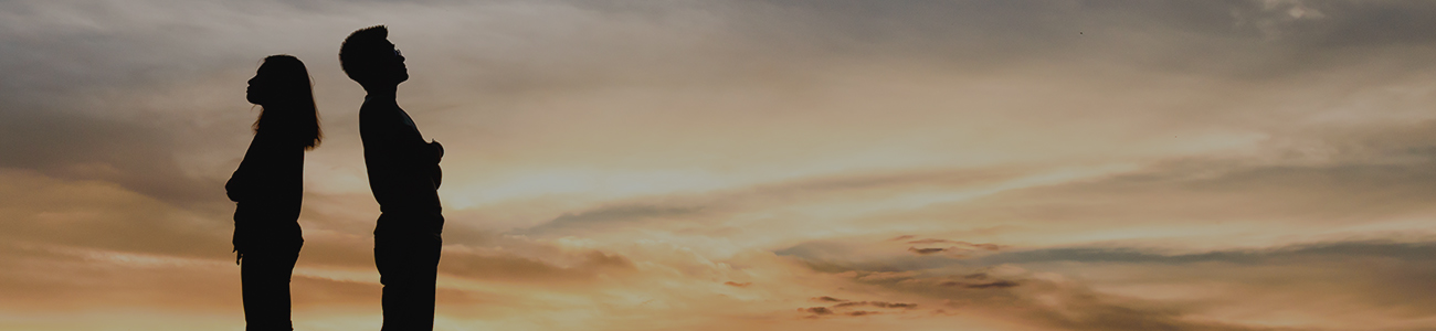 Silhouette of couple standing back to back in from of a sunset.